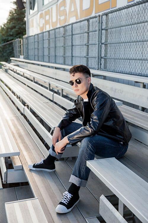 50s Sock Hop Outfits for Guys – How to Rock Retro Style This may contain: a man sitting on top of a wooden bench next to a bleachers field
