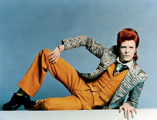 This may contain: a man with red hair sitting on the ground wearing yellow pants and a colorful jacket